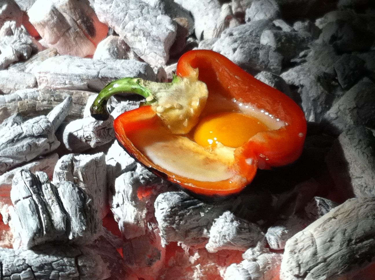 Halbe rote Paprika mit rohem Ei, bereit zum Garen direkt in der Glut